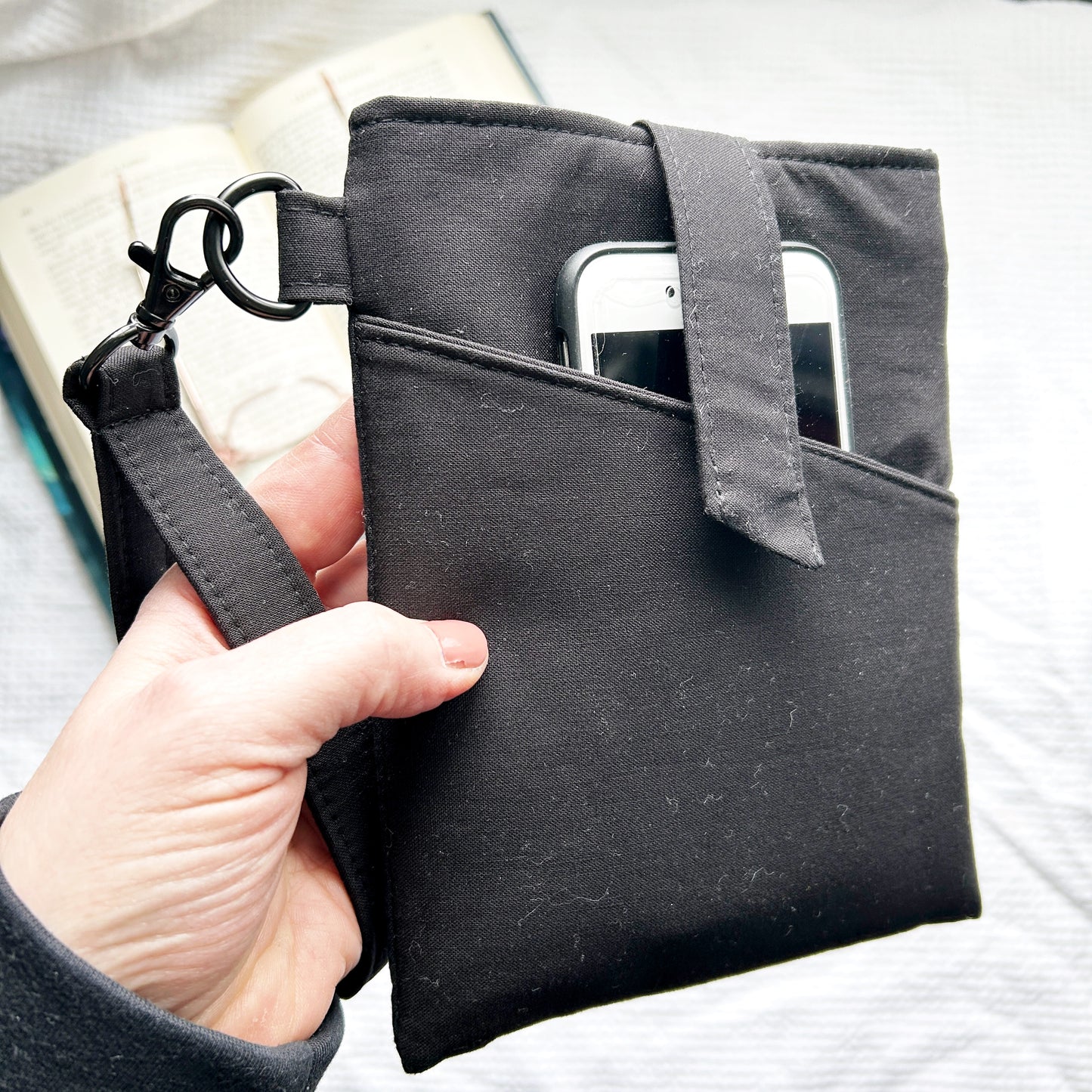 Black pouch with a strap held by a hand, containing a smartphone.